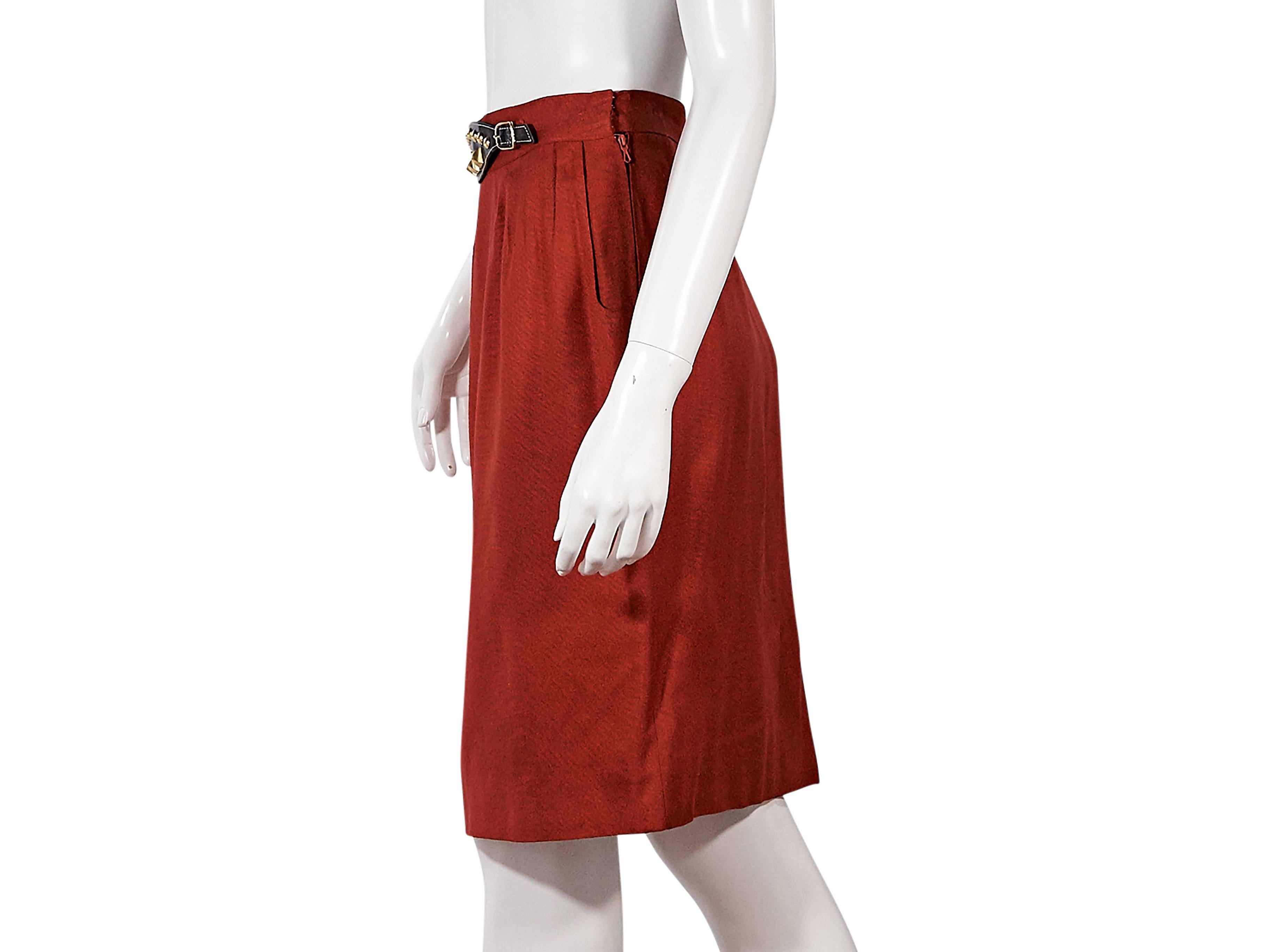 Product details:  Red vintage pencil skirt by Hermès.  Banded waist accented with faux belt buckle.  Pleats taper off waist.  Concealed side hook and zip closure.  Back center hem vent.  Goldtone hardware.  Label size FR 40. 
Condition: Pre-owned.