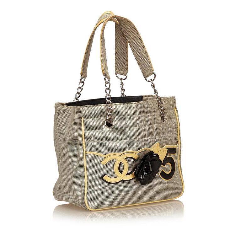 Product details:  Beige quilted canvas Camellia No. 5 tote bag by Chanel.  Trimmed with yellow leather.  Front applique accents.  Dual shoulder straps.  Open top.  Lined interior with inner zip pocket.  Protective metal feet.  Silvertone hardware. 