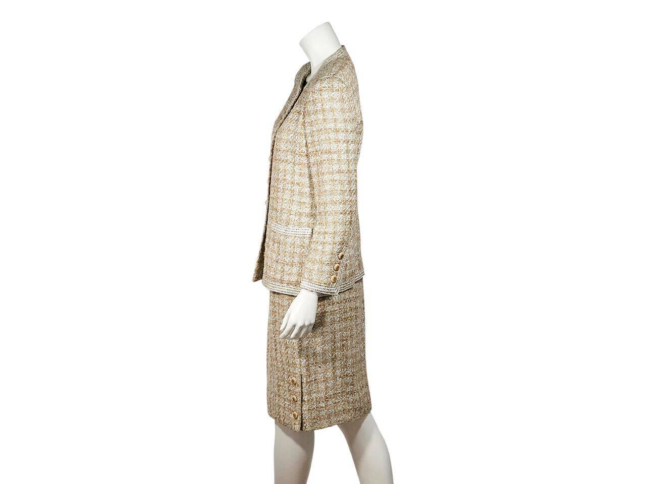 Product details:  Vintage tan and white tweed wool skirt suit set by Chanel.  Crewneck.  Long sleeves.  Button-front closure.  Waist patch pockets.  Matching skirt.  Concealed back zip closure.  Button detail at side hem.  Label size FR