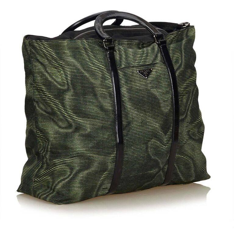 Product details:  Green nylon tote bag by Prada.  Trimmed with black leather.  Top carry handles.  Detachable, adjustable crossbody strap.  Top zip closure.  Lined interior with inner zip pocket.  Front exterior slide pocket.  Protective metal feet.