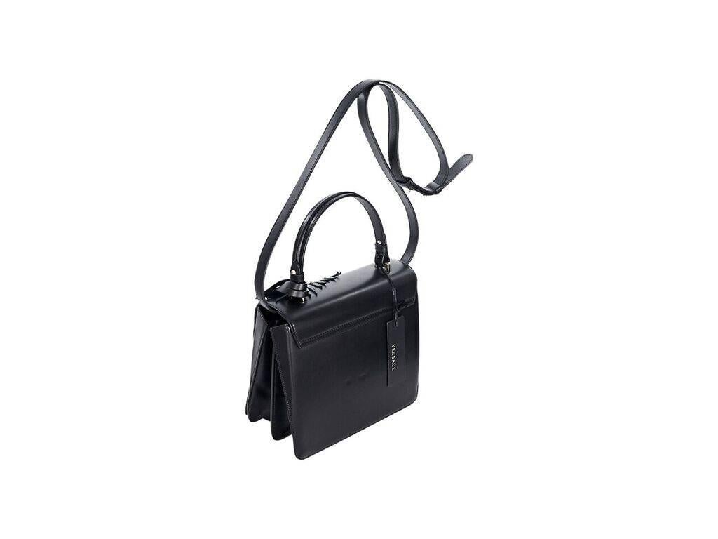 Product details:  Black leather mini satchel bag by Versace.  Features a studded and embellished front.  Top carry handle.  Detachable, adjustable crossbody strap.  Hanging luggage tag.  Front flap with clasp closure.  Lined interior with center zip