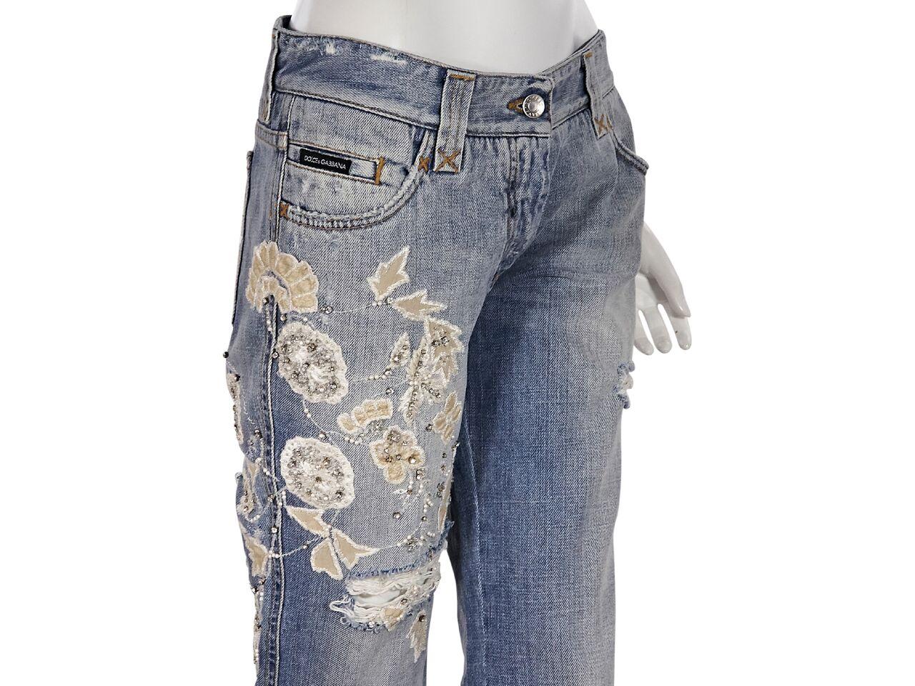 Product details:  Light wash distressed jeans by Dolce & Gabbana.  Embellished with crystals and floral applique.  Five-pocket design.  Looped waist.  Button and zip fly closure.  32.5