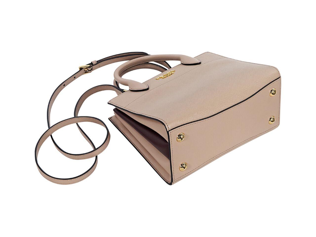 Product details:  Light beige saffiano leather satchel by Prada.  Dual carry handles.  Detachable, adjustable crossbody strap.  Open top.  Leather lined interior with inner open compartments and inner slide pocket.  Protective metal feet.  Goldtone