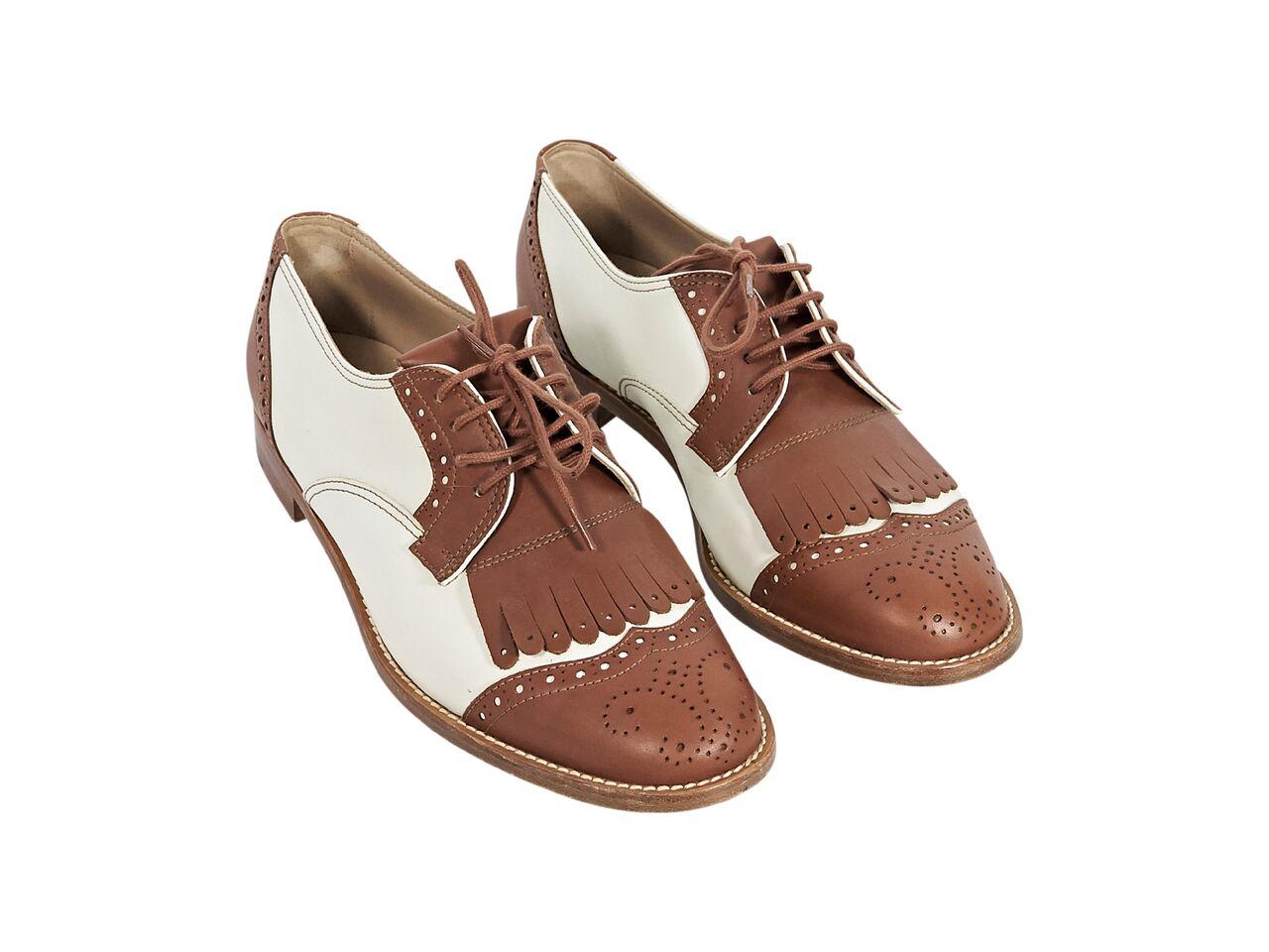 Product details:  White and brown leather oxfords by Manolo Blahnik.  Lace-up closure.  Round wingtip toe.  Low stacked heel.  1