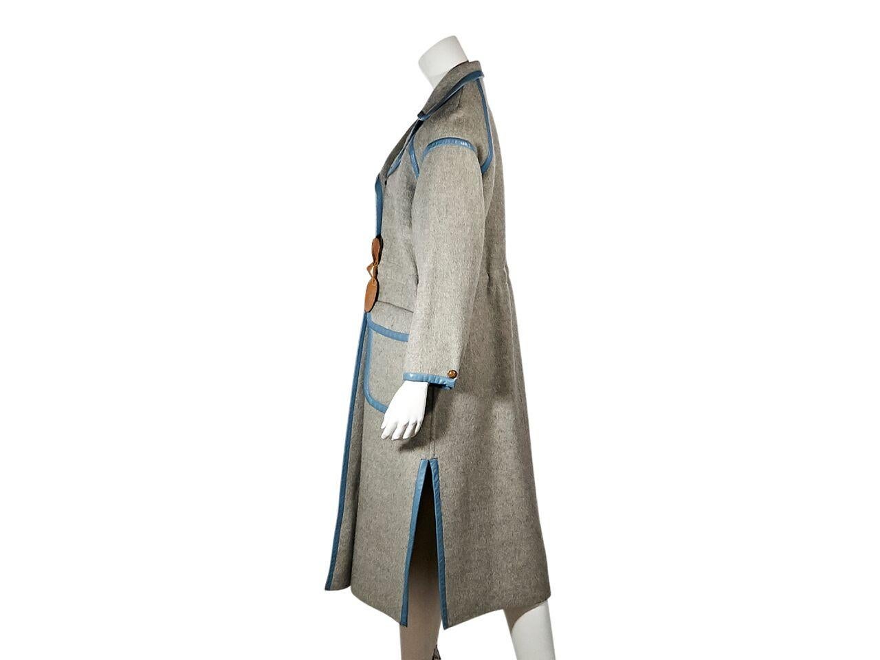 Product details:  Vintage grey wool coat by Courreges.  Trimmed with blue leather.  Rounded notched lapel.  Long sleeves.  Double-breasted button front.  Drawstring waist with bow ends.  Waist flap pockets.  Side hem slits.  43
