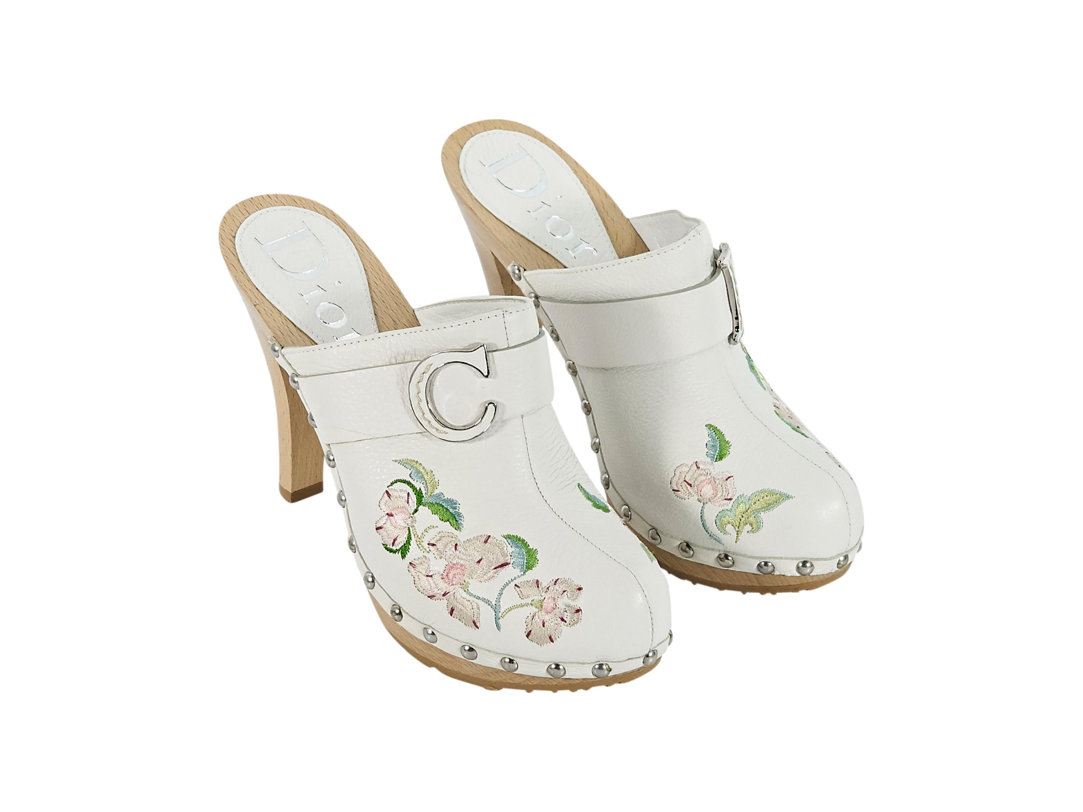 Product details:  White leather heeled clogs by Christian Dior.  Floral embroidered design accented with studs.  Round toe.  Wooden stiletto and low platform.  Slip-on style.  Silvertone hardware.  4.5