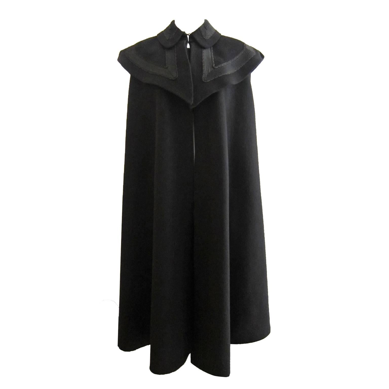 Elegant black wool cape from circa 1970s. With detailed extra pieces over the shoulders with ribbons and embroidery.  
Fully lined.
One size fits most.
Measurements:
Shoulders : 48 cm
Length 110 cm