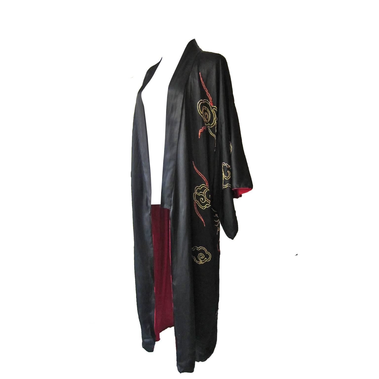 Black satin kimono style robe featuring dramatic gold embroidery from circa 1940s. 
Futures two large dragons flying among the clouds over Fuji mountain, beautifully embroidered with thick metallic gold chord. With contrasted bright red lining.