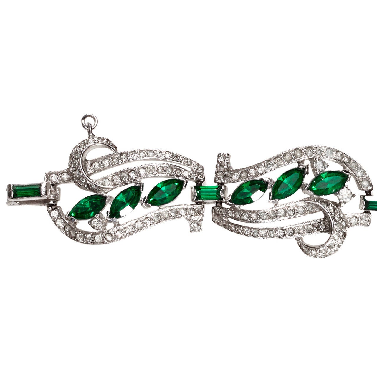 A fantastic emerald and clear crystal rhinestone bracelet by Kramer of New York.

The delicate undulating openwork design is rhodium plated and made up of six articulated panels, decorated with curlicue shapes and emerald navette shaped