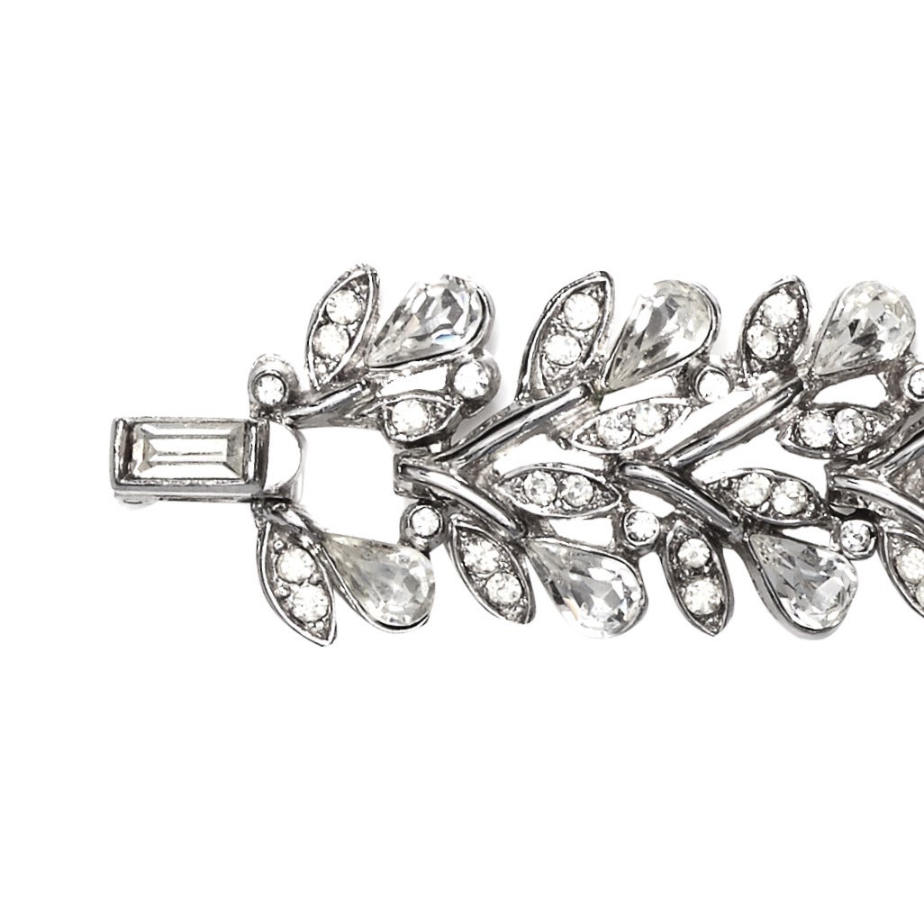 A beautiful rhodium plated silver tone bracelet by Trifari.
The delicate design is reminiscent of flowers and foliage, each leaf is embellished with crystal rhinestones and the teardrop shaped stones emulate flower buds, it is made up of 10