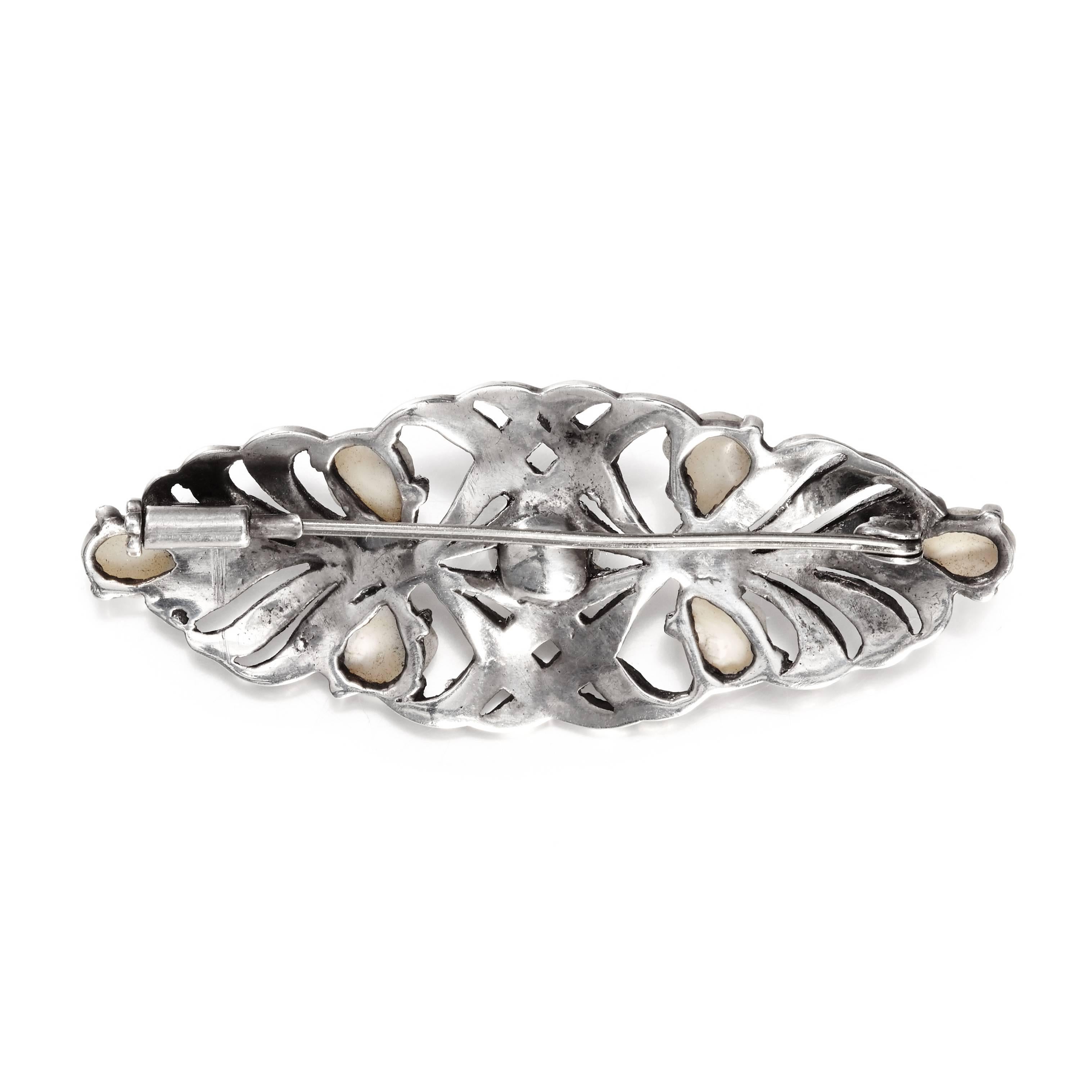 A beautiful openwork brooch in the shape of an elongated oval. The delicate lace like design is created on a dark oxidised silver base, set with marcasite and blister pearl accents around a central pearl focal.

The condition is excellent and the