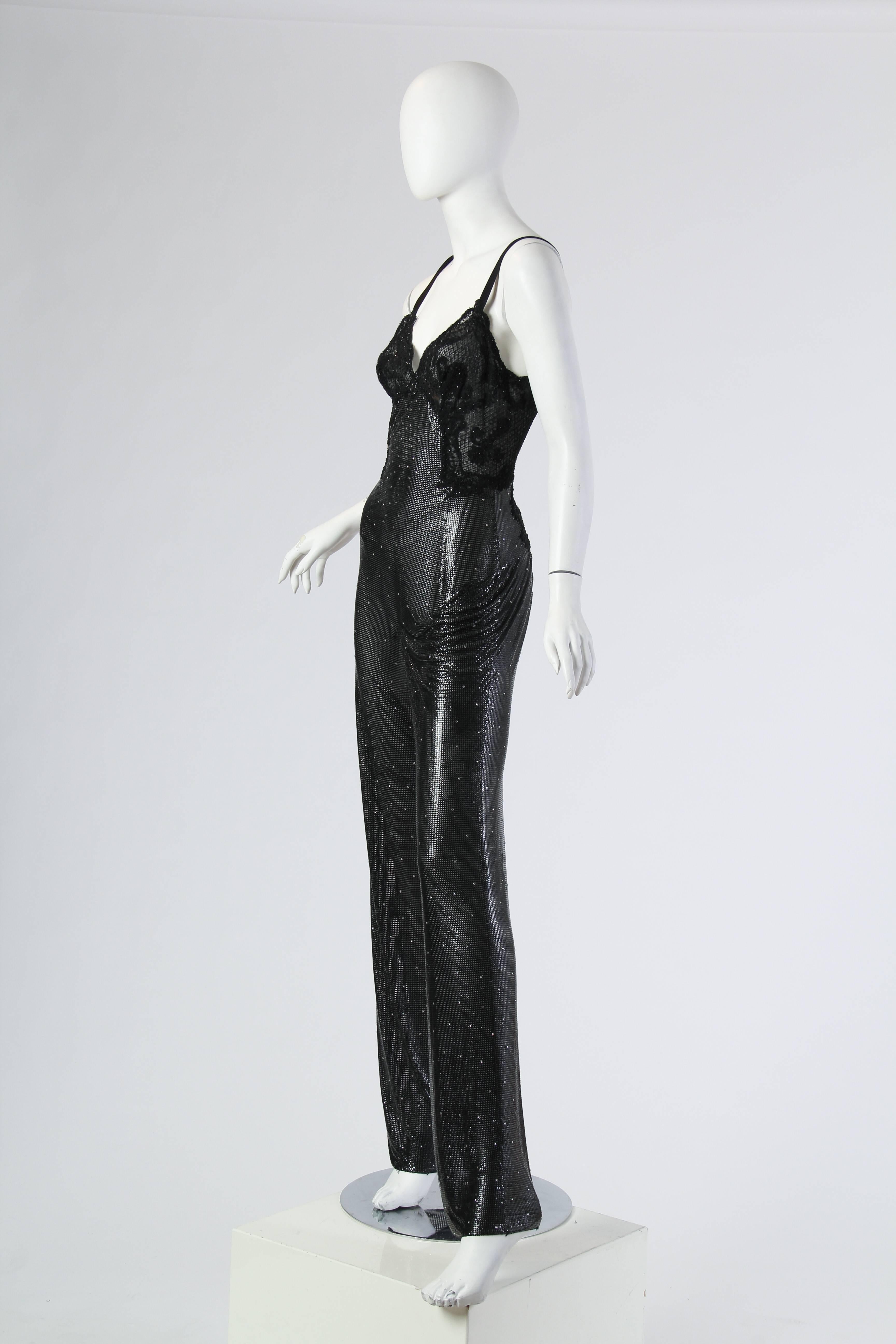 This is a striking metallic mesh jumpsuit by famed designer Gianni Versace. The straight-legged number is fitted through the hips, glimmering attractively over the body's curves and appearing to lengthen the body with its clever seaming. The bust