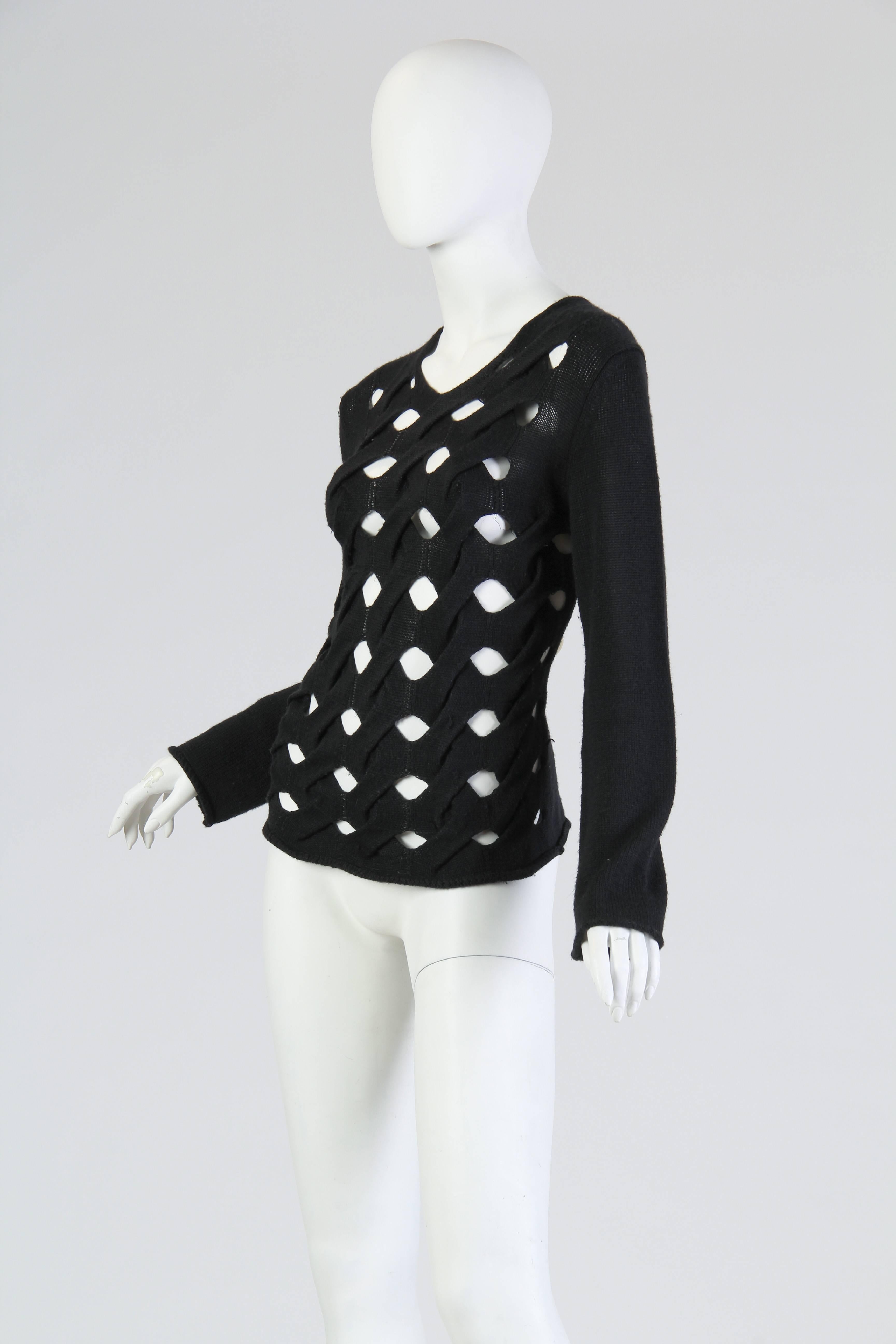 This black knit top, made by avant-garde giant Comme des Garçons, is intricately fashioned in a cable-like texture which gives the appearance of scrolling vines or window panes. The lines of knit are entirely interconnected, but twist diagonally