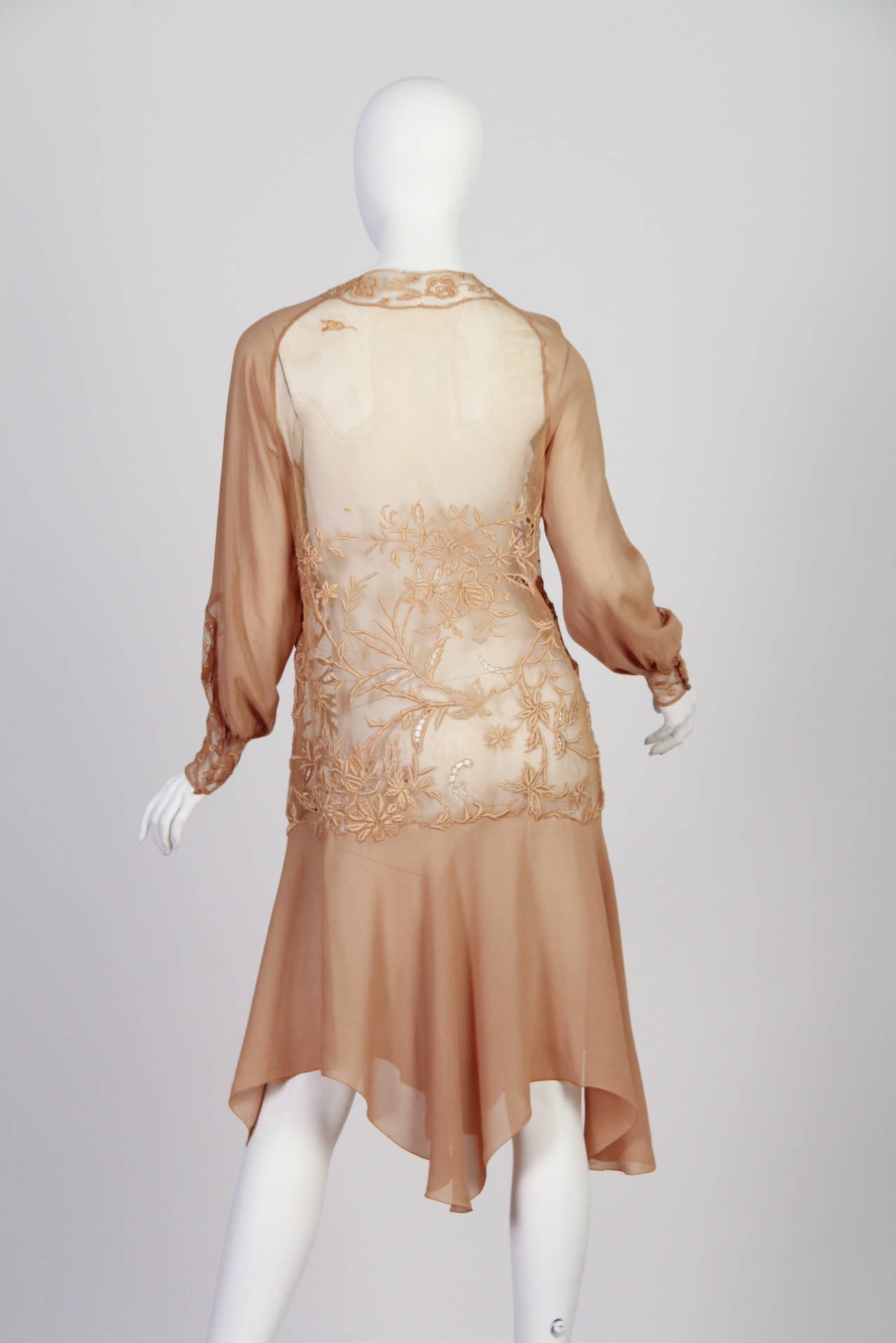Embroidery of the finest work abounds in the most interesting and inspired of ways in this dress from the mid 1920s. The age was art deco but this dress harkens back to more romantic of times. The body of the dress is made from very fine net which