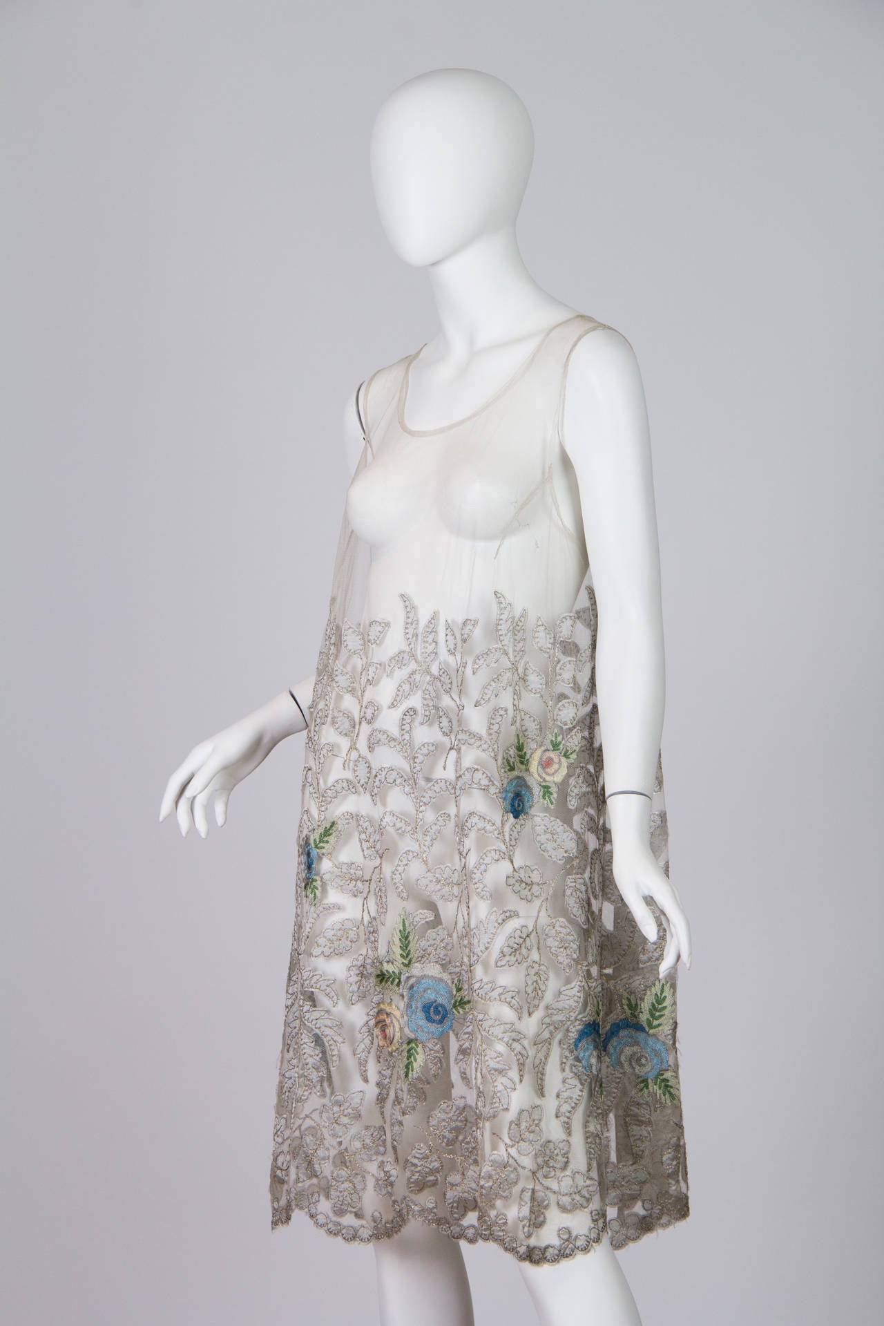 The finest silk net has been appliquéd with silk leaves, chain stitch embroidered in silver lamé thread with colorful flowers scattered about. In very fine near mint condition. A true beauty and unique technique from the 1920s.