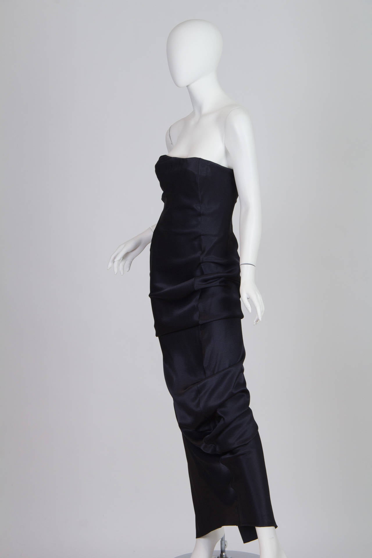 This is a beautiful evening gown by John Galliano. The shimmering navy satin is artfully draped about the hips and legs to add texture and interest to an otherwise classic gown. The bodice is fully constructed allowing the bias crepe back satin to