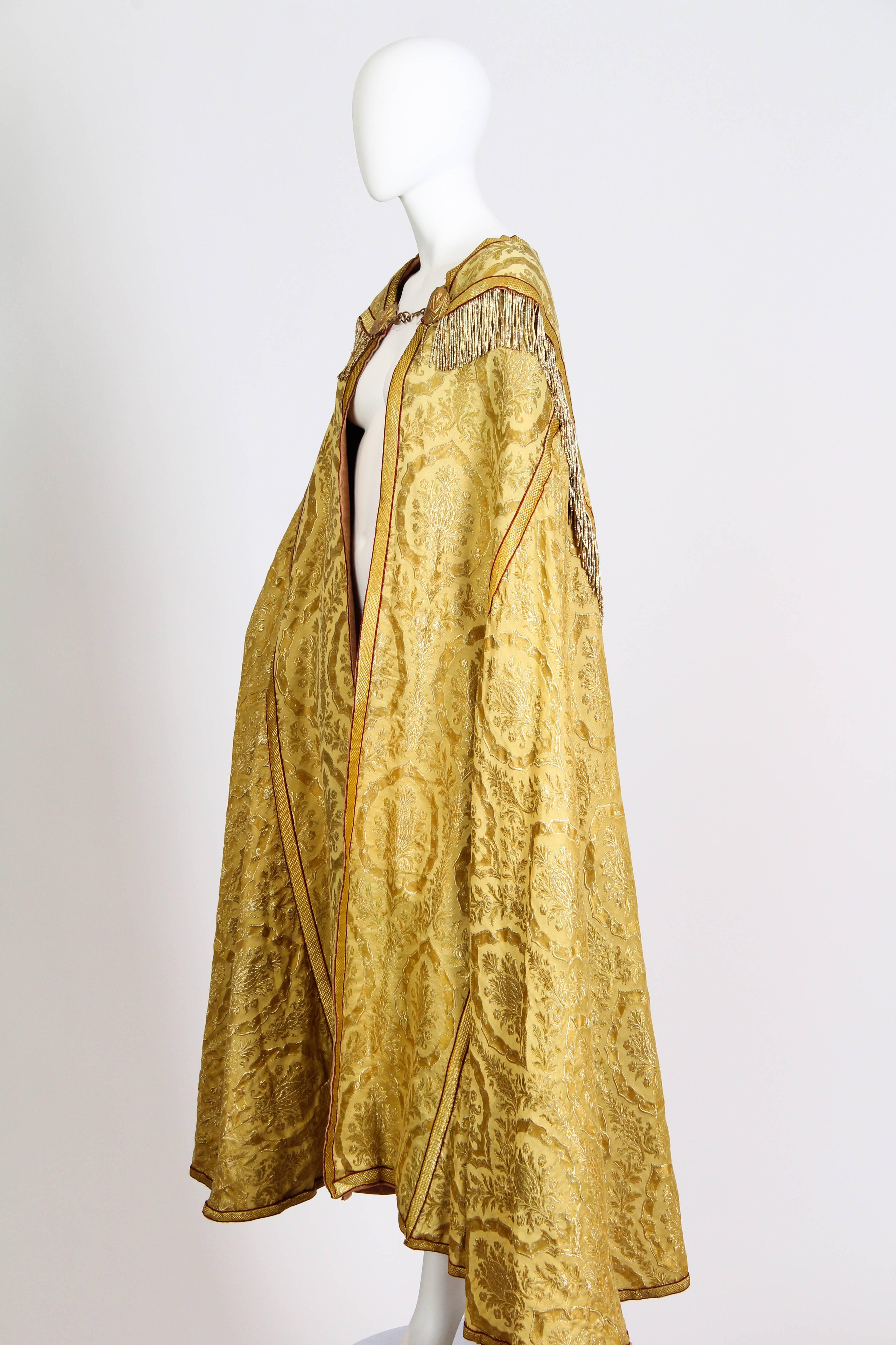 Dating from the first half of the 20th century this cape is most likely of religious origin. With angels cast in the clasp as well as the cloth is of the heavy types of tapestries used in ecclesiastical garments. The textile is woven with a cotton