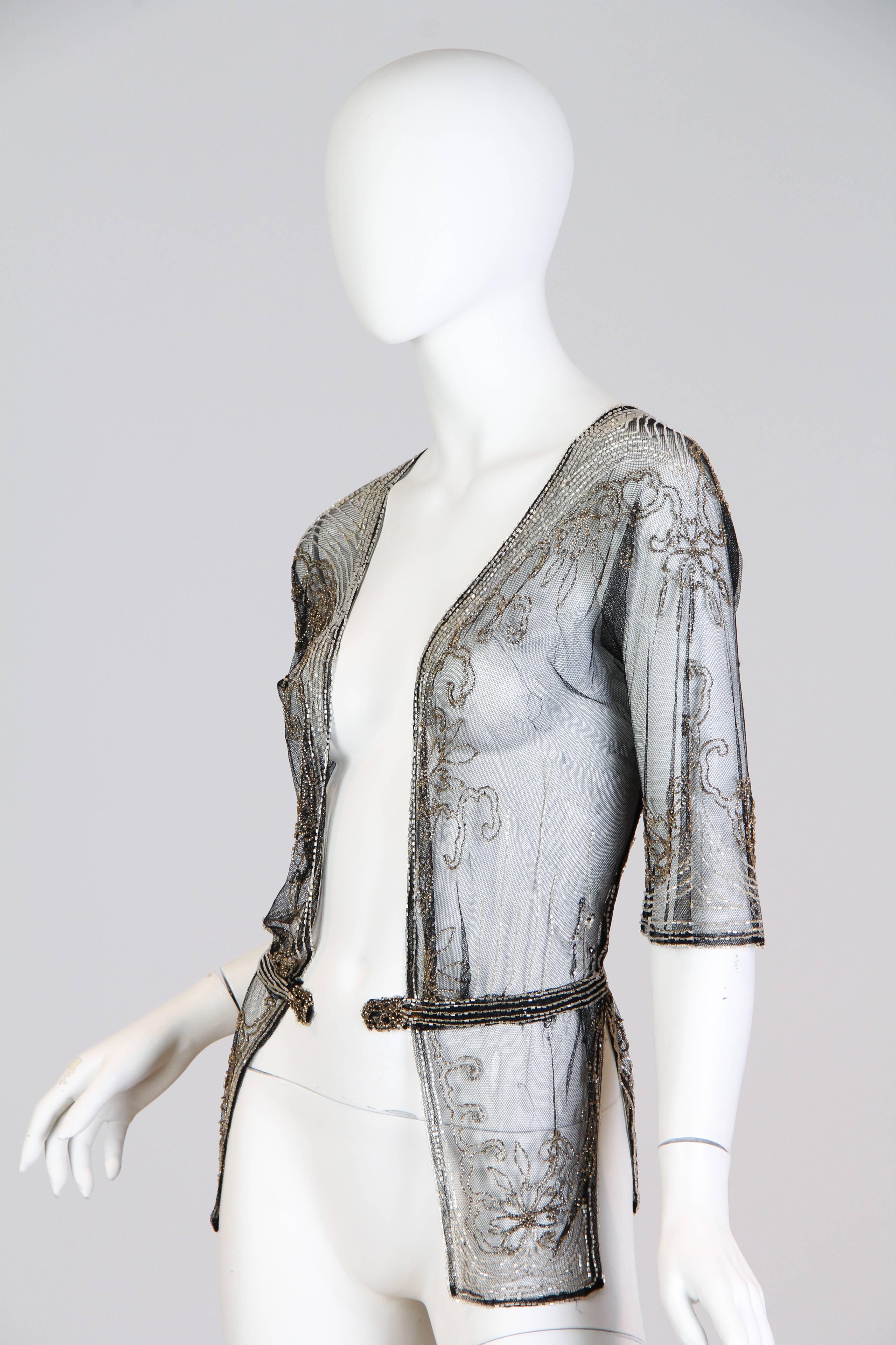 This is an incredible jacket from the 1920s. Made of a light-as-air black chiffon net with silver embroidery, this piece shows the amazing delicacy and attention to detail which characterizes the 1920s. Sometimes called the 