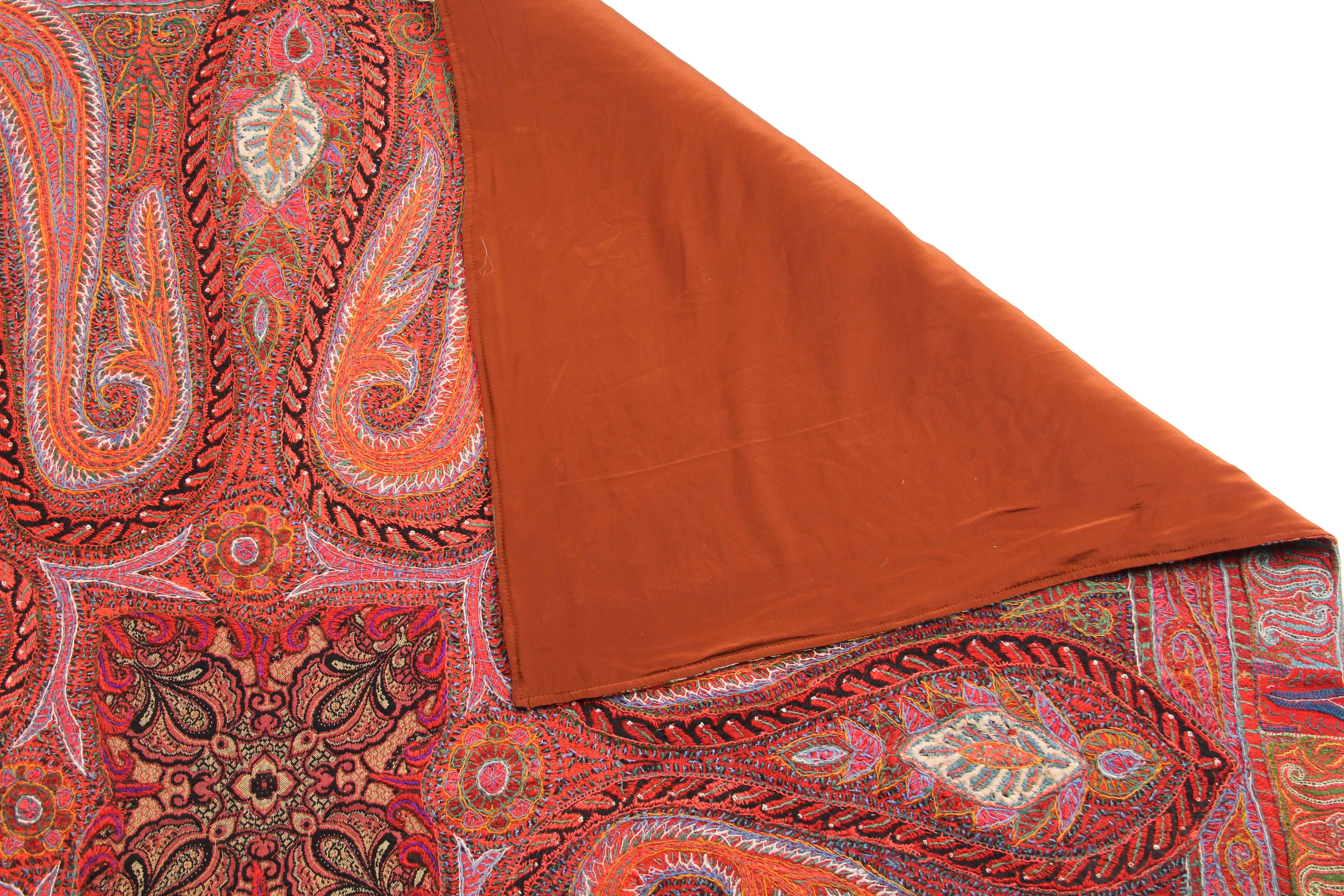 This is a stunning paisley scarf covered in intricate embroidery. The crewelwork is done in strands of wool floss worked over a red twill base, and a pumpkin silk lining hides the back side of the embroidery and gives the scarf a smooth and