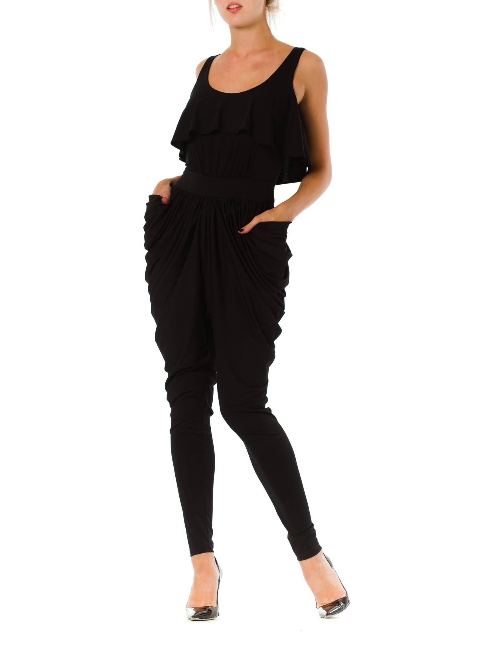 This gathered jumpsuit is an avant-garde number by famed designer Alexander McQueen. The hourglass-shaped garment is anchored by its wide, smooth waistband, from which the heavily gathered legging portion extends out over the hips. The voluminous