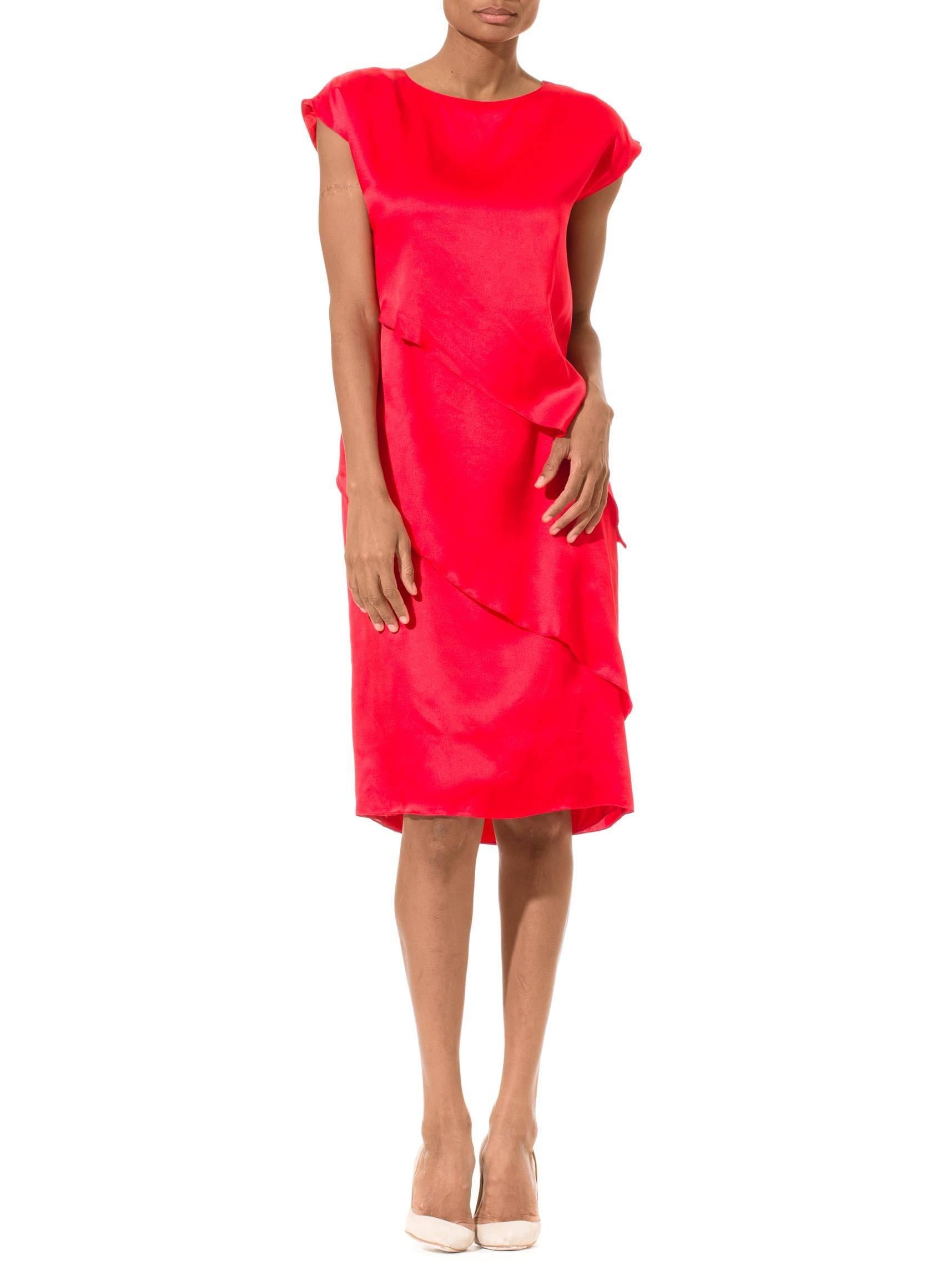 This is a gorgeous silk-satin dress by Pierre Cardin, in a bold scarlet hue. The silhouette is simple, with a straight shape falling to the knees, a demure neckline, and cap-length sleeves cut in one with the dress. The simplicity of the silhouette
