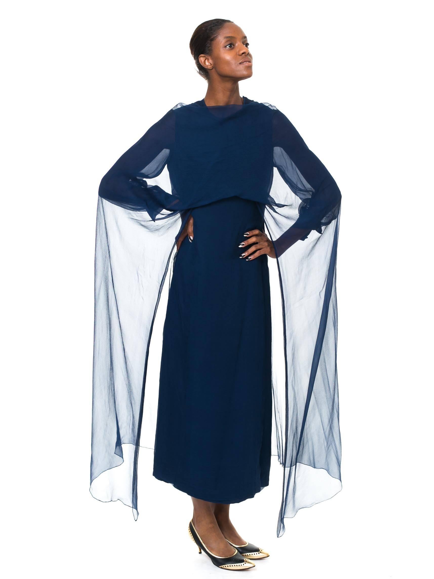 This is a midnight blue Balmain evening gown with full, cuffed sleeves and a wonderful detachable chiffon mantle, which extends in a full cape down the sides. The cut of the dress is a simple and elegant column cut, giving the impression of height