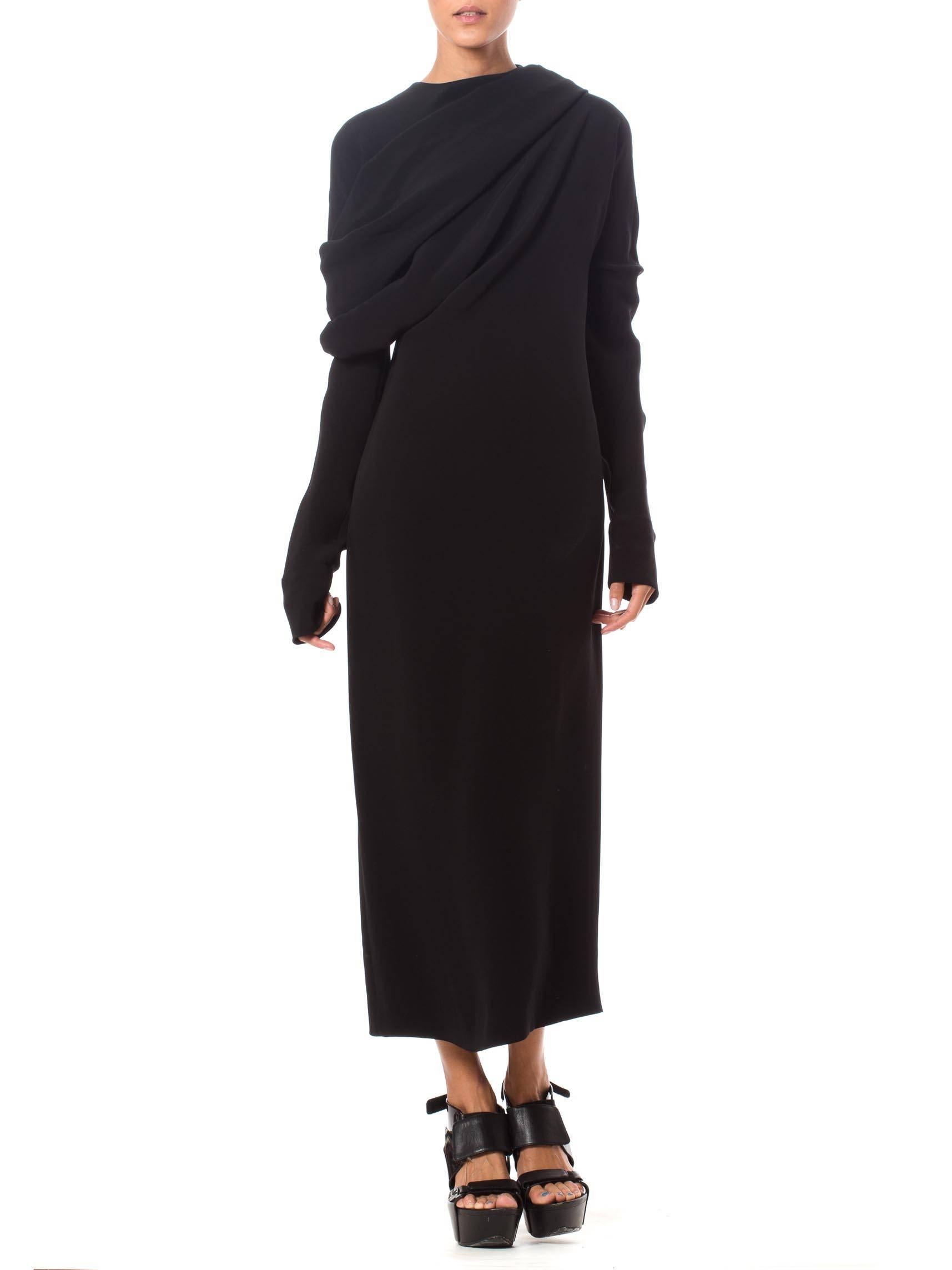 This is an elegant black dress with extra-long sleeves and an asymmetrical draped detail across the shoulders and bust, genius in pattern cutting and draping. The overall silhouette of the dress is simple and classic, while the careful draping on