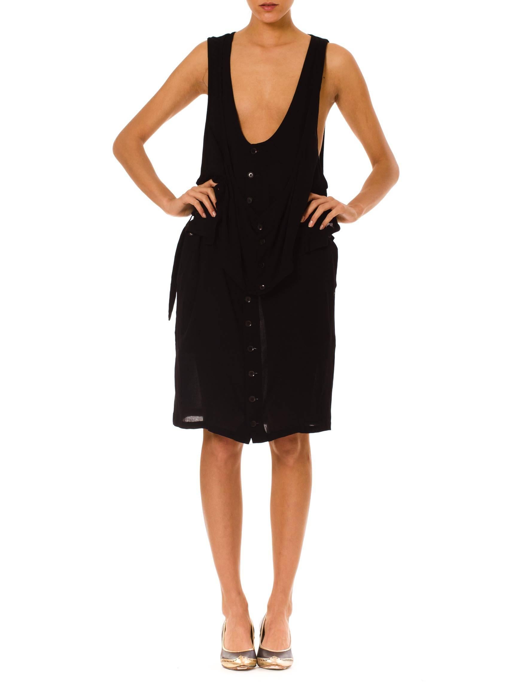 This is a double-layer black dress with buttons down the front and an edgy draped silhouette. The bottom layer has a semi-sheer lined skirt and extra-long straps, so that the neckline hangs low on the ribcage. Intended to be worn over a tank or