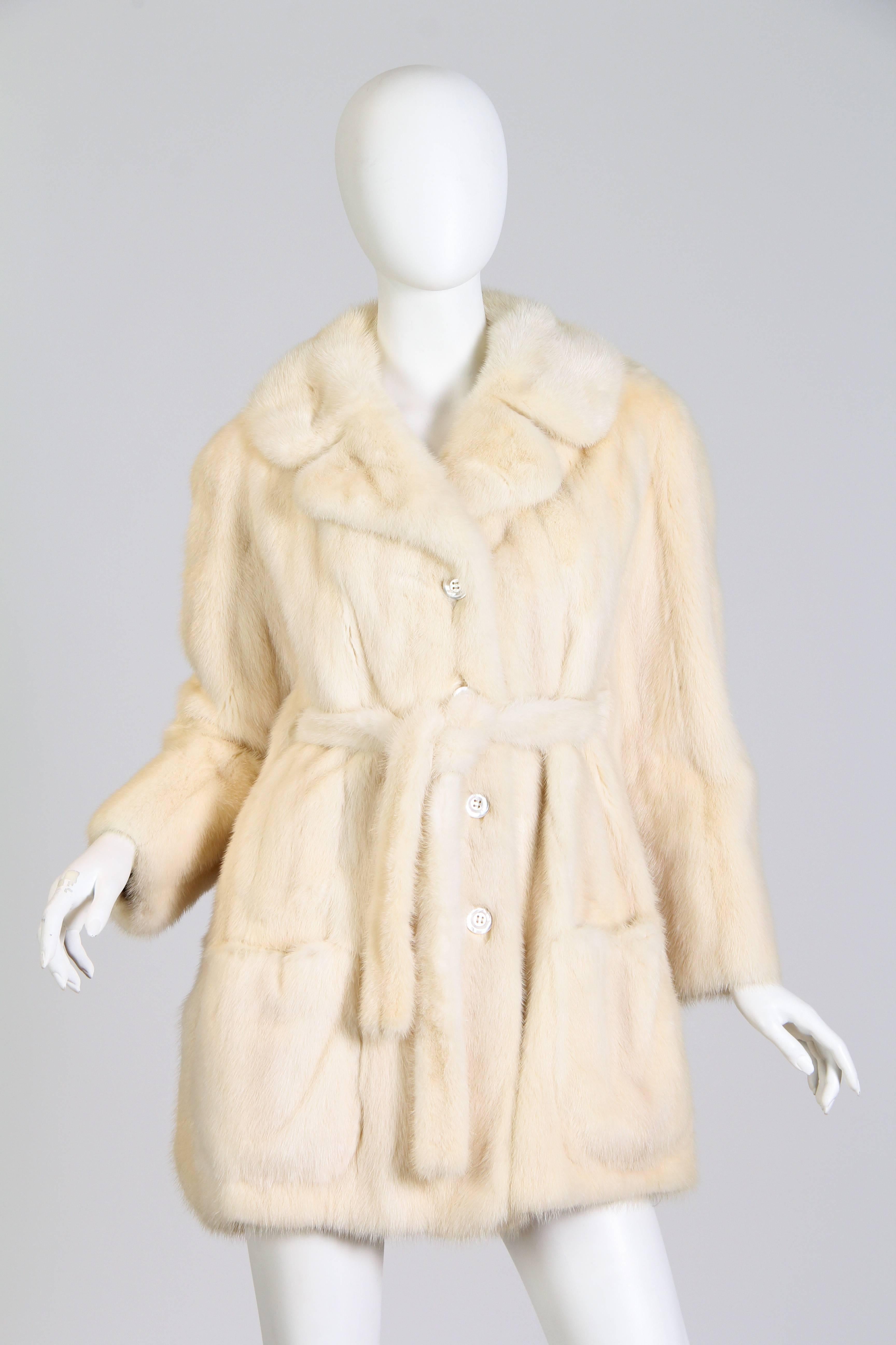 This is a beautiful mink fur coat by Bullocks Wilshire. The hip-length coat has a classic 1960/70s walker silhouette, with straight sleeves and a wide, deeply notched collar. Thick white mother of pearl buttons close up the front and large patch