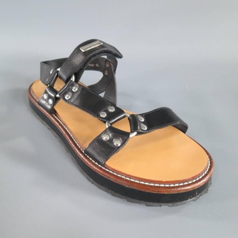 These unique runway sandals by DSQUARES2 comes in a black leather and feature fetish harness inspired straps with silver tone studs and O hoops, ankle harness, velcro closure with silver tone engraved plaque, and thick black sole with brown leather