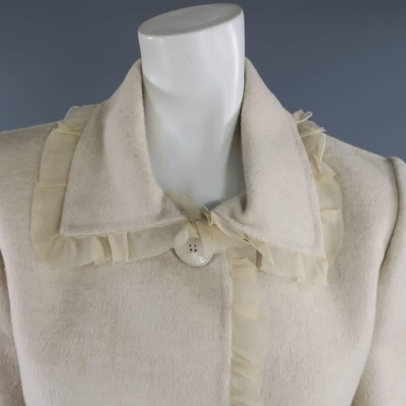 This gorgeous OSCAR DE LA RENTA jacket comes in a light peachy beige orylag cashmere wool blend and features a pointed collar with light peachy pleated, raw edge chiffon, three button closure, and cutout illusion sheer stripe panels at the hem.