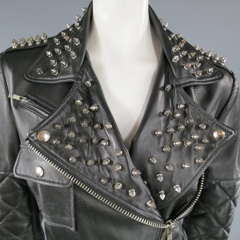 This fierce SIMONE by KATIE NEHRA biker jacket comes in smooth soft black leather and features a cropped retro fit, asymmetrical zip, patch pocket, belted waist, epaulets,  quilted sleeves, and silver tone spike stud embellishments. Made in The