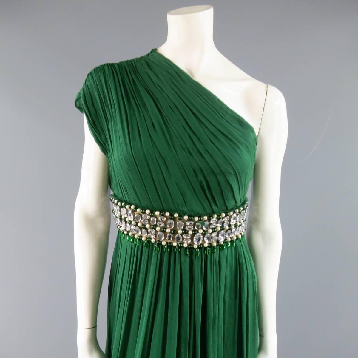 This stunning NAEEM KHAN evening gown comes in emerald green silk crepe chiffon and features a pleated one shoulder bodice, flowing layered pleat skirt, and beige fabric embellished waist with raw edge, faux pearl and rhinestone jewel