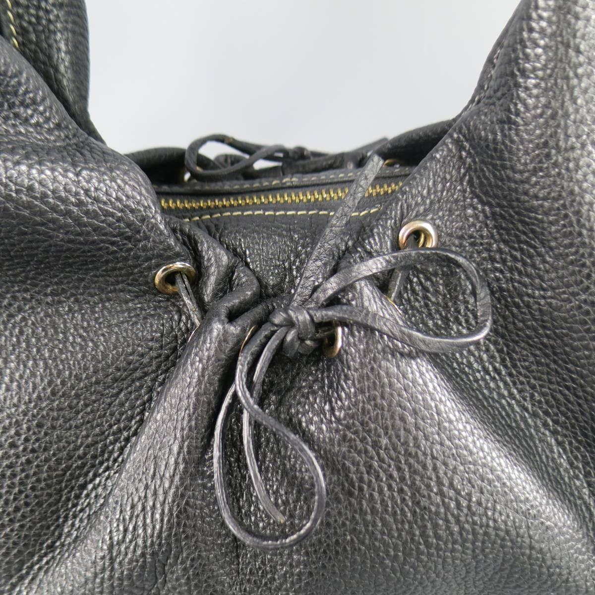 This lovely BOTTEGA VENETA hobo bag comes in smooth black pebble textured leather and features a contrast stitch shoulder strap with gold tone hoops, gathered middle with grommets and woven leather ties, side grommets braided leather engraved