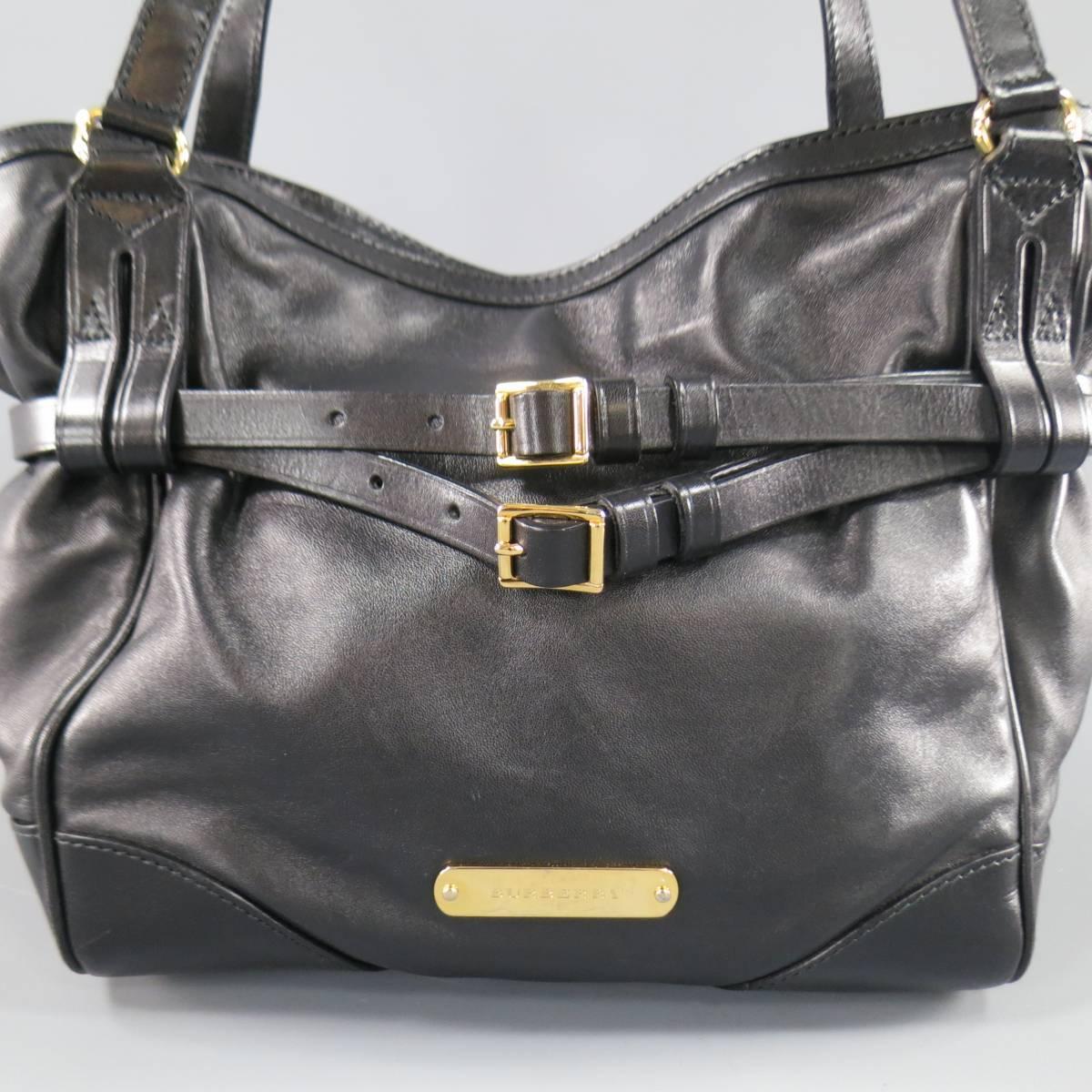 This unique BURBERRY tote bag comes in soft black leather and features a gold tone engraved logo plaque, double top handles, cinched top with double skinny belts, snap closure, and signature plaid interior. Made in Italy.
 
Excellent Pre-Owned