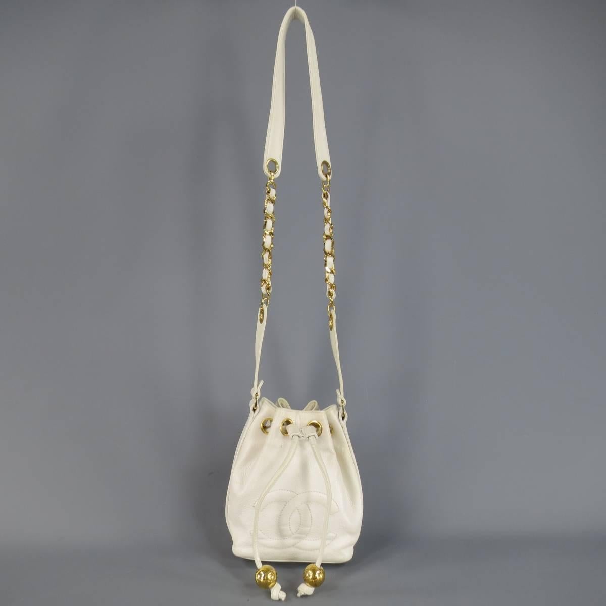 This fabulous 1980's vintage CHANEL mini bucket bag comes in white pebbled leather and features an oversized embroidered CC logo, drawstring closure with yellow gold tone grommets and braid textured beads, chain and leather shoulder strap and