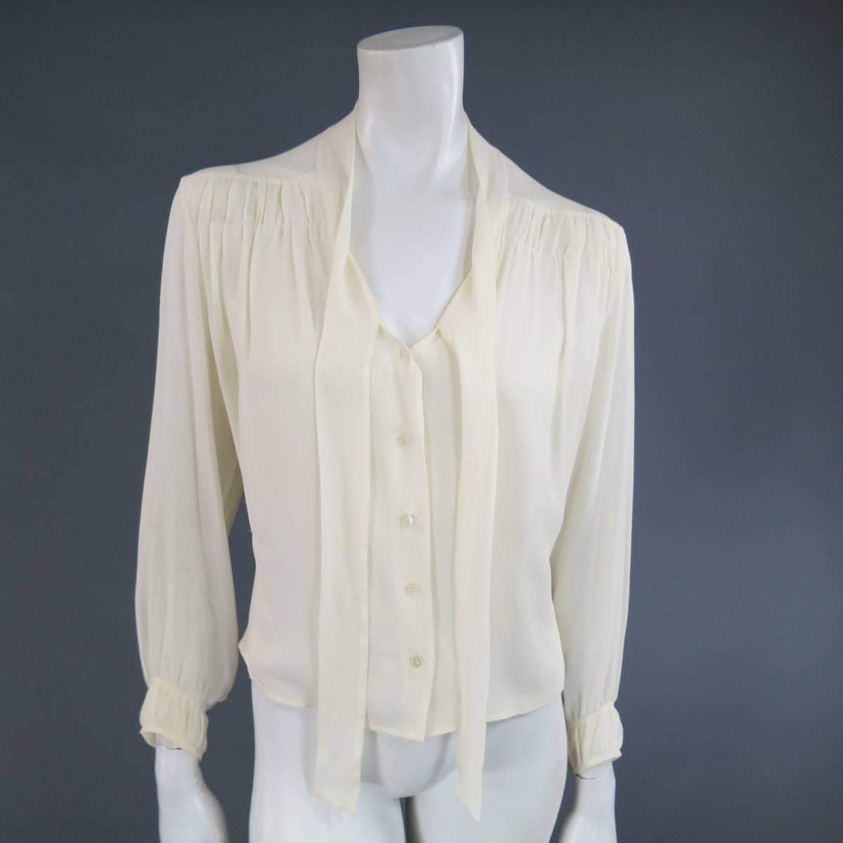 This gorgeous vintage HERMES blouse comes in an off white cream silk textured sheer chiffon and features a v neck, button up front, sheer panel shoulders, gathered back, gathered cuffs, and a tied bow. Minor discolorations on neck. Made in France.
