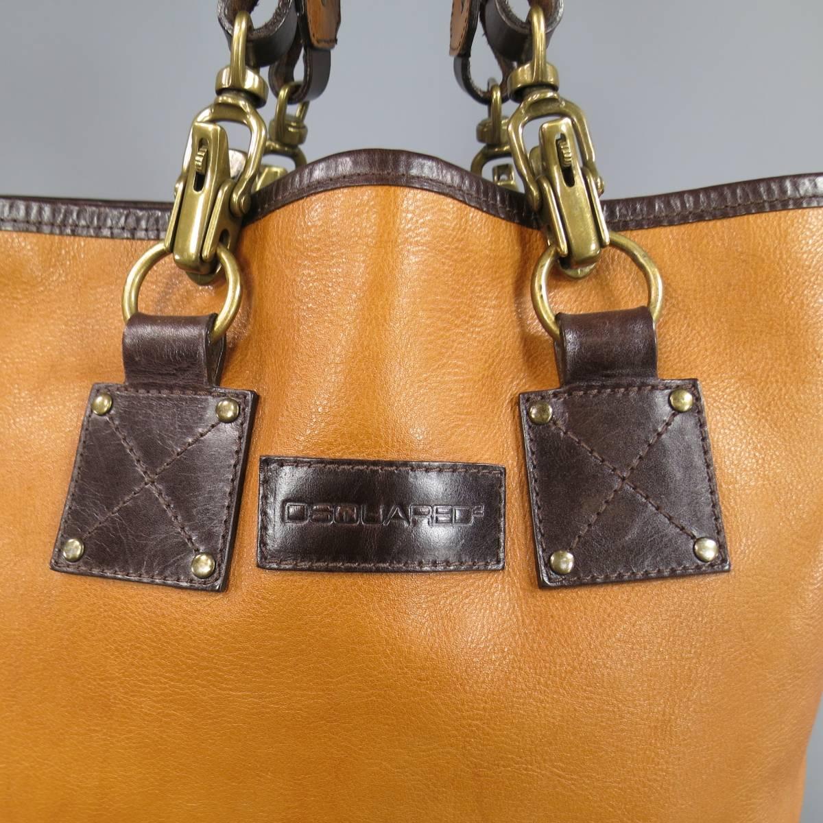 DSQUARED2 tan leather tote bag featuring chocolate brown trim and details, double perforated logo top handles with dark gold tone metal clasp hardware and belted side details. Wear throughout leather. Tag cut out of lining. As-Is. Made in Italy.
