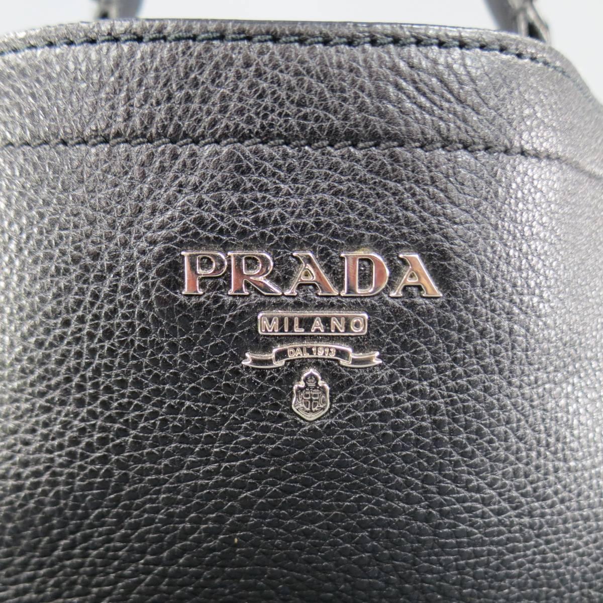 Classic PRADA shoulder bag in black pebbled leather featuring symmetrical side pockets, frontal silver tone metal logo plaque, snap closure, and adjustable shoulder strap with hoops. Made in Italy.
 
Excellent Pre-Owned Condition.
