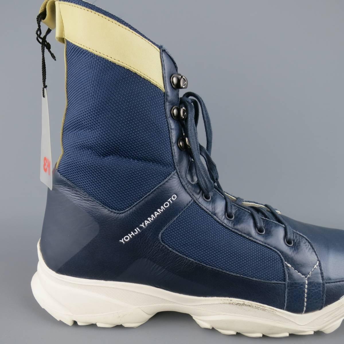 Y-3 Adidas by YOHJI YAMAMOTO combat boots come in a navy blue smooth leather and feature a navy mesh shaft, beige leather trim, lace up front with gunmetal ski hooks, and thick white rubber sole. New with scuff on sole from storage. As-Is.
