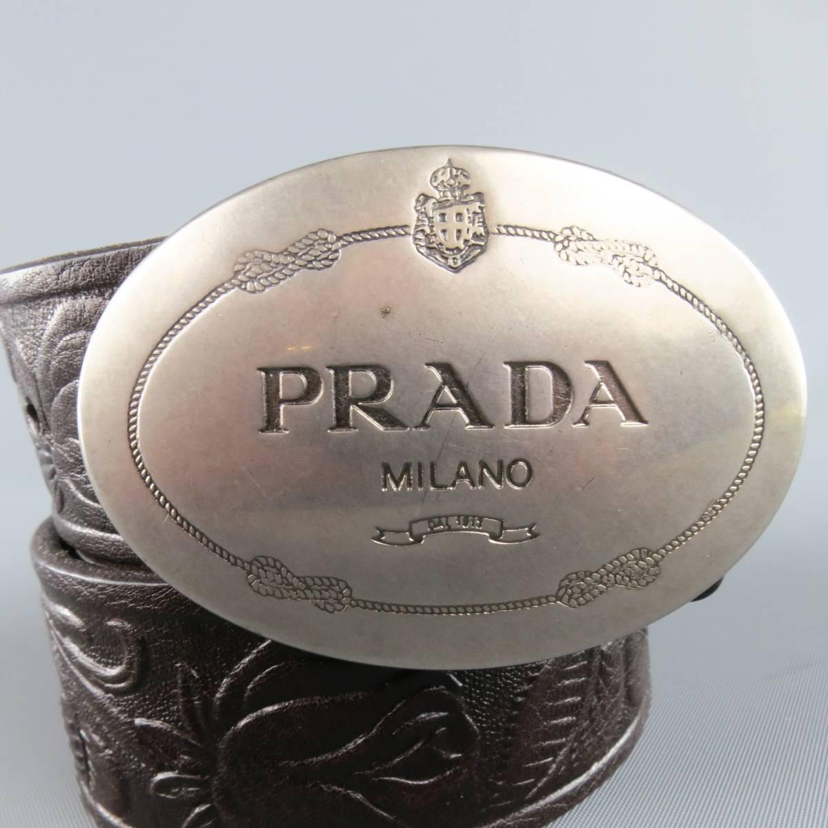 PRADA belt features a floral embossed chocolate brown leather strap and silver tone engraved logo oval shaped buckle. Made in Italy.
 
Good Pre-Owned Condition.
Marked: 8 40/100
 
Length: 47.5 in.
Width: 1.5 in.
Fits: 39-43 in.
Buckle: 3 x 2 in.