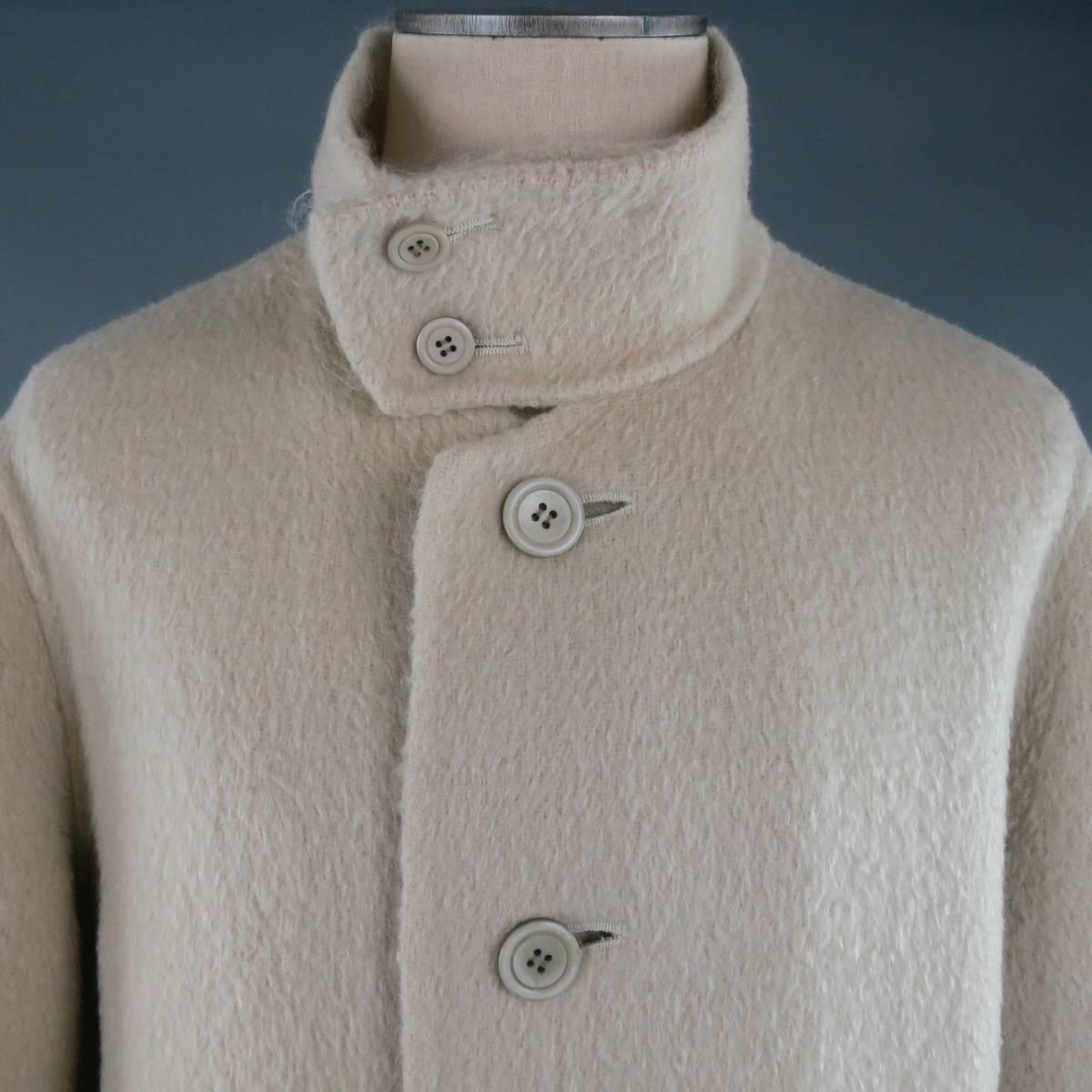 ISSEY MIYAKE Coat consists of wool blend material in a cream color tone. Designed in a oversize style, button-up front and bottom patch pockets. Detailed with a high collar button closure. Fuzzy texture with cropped sleeves. Made in Japan.
