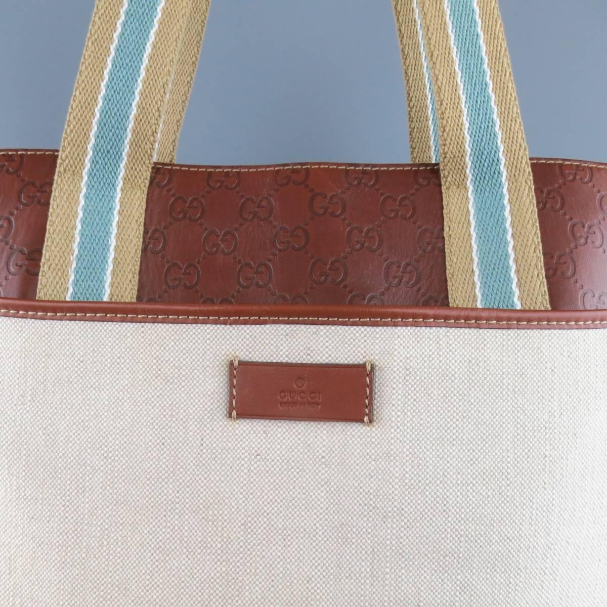 GUCCI tote bag comes in light beige canvas and features tan brown Guccissima monogram embossed leather, front and back snap pockets, internal storage pockets, and beige and teal stripped webbing handles with leather grips. Wear throughout leather