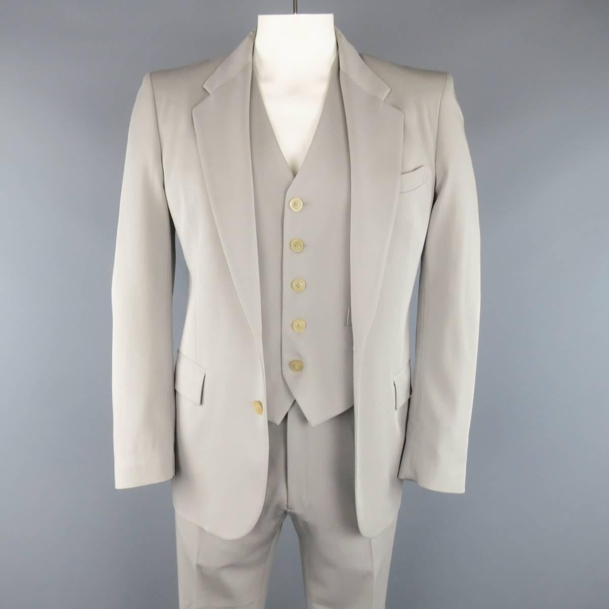 Three piece MAISON MARTIN MARGIELA suit in a light muted gray wool twill includes a two button, notch lapel sport coat with functional button cuff, v neck vest, and matching flat front trousers. Seam coming undone on back. As-Is. Made in Italy.
