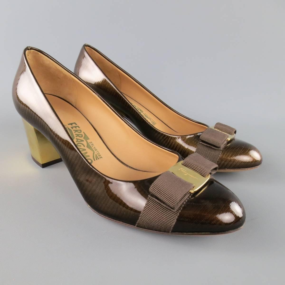 SALVATORE FERRAGAMO pumps come in a glossy brown lizard patent leather and feature a gold tone engraved plaque with ribbon bow and metallic gold tone chunky heel. Never worn but minor imperfections. Made in Italy.
 
Excellent Pre-Owned
