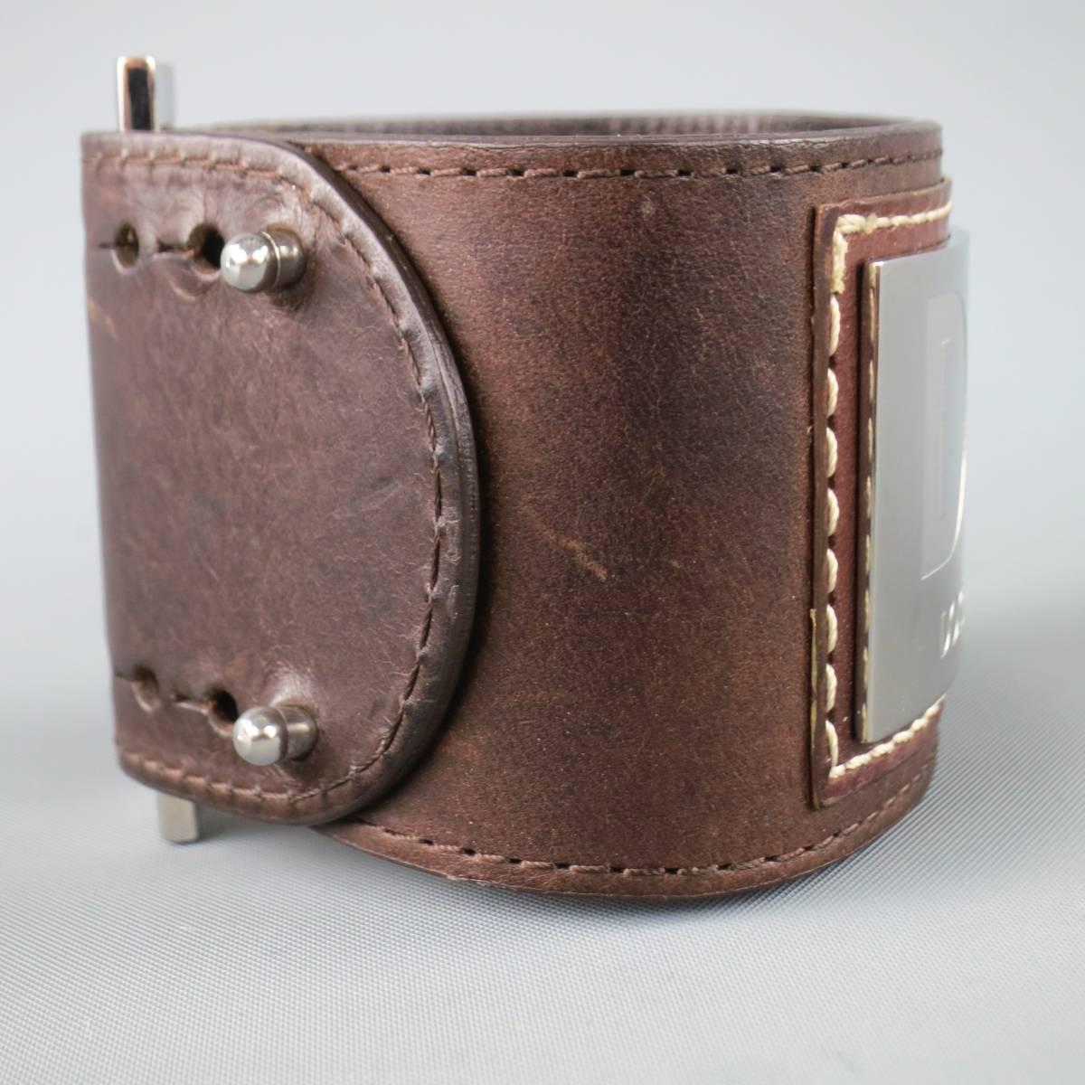 D&G by Dolce & Gabbana cuff comes in a rich chocolate brown leather and features an oversized silver tone logo plaque and adjustable button stud closure. Wear throughout. Made in Italy.
 
Good Pre-Owned Condition.
 
Length: 8 in.
Width: 1.75