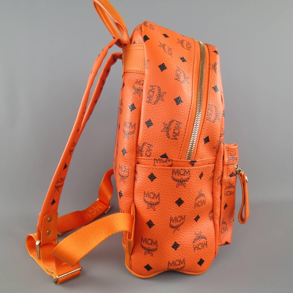 MCM backpack comes in orange coated canvas faux leather with all over black MCM logo print and features a frontal pocket, side pockets. gold tone engraved plaque, silver pyramid studs, and top zip closure. Wear throughout. As-Is.
 
Good Pre-Owned