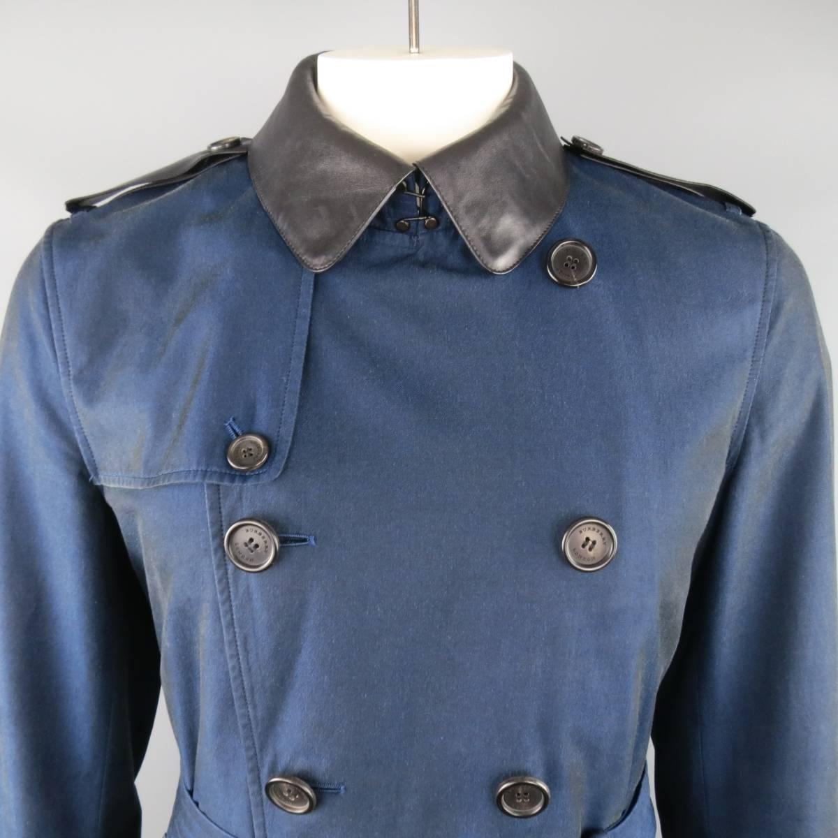 BURBERRY LONDON tranch coat comes in a navy blue cotton with a sharkskin iridescent sheen and features a double breasted button front, storm flap, belted waist, and black leather collar, epaulets, and and buff belts. Detachable leather collar. Made
