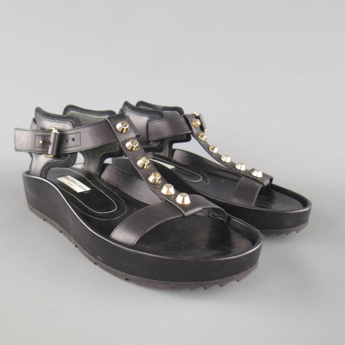 BALENCIAGA flat sandals come in smooth black leather and feature a thick platform sole with covered leather sides, padded ankle harness, and T strap with gold tone studs. With box. Made in Italy.
 
Excellent Pre-Owned Condition. Retails at