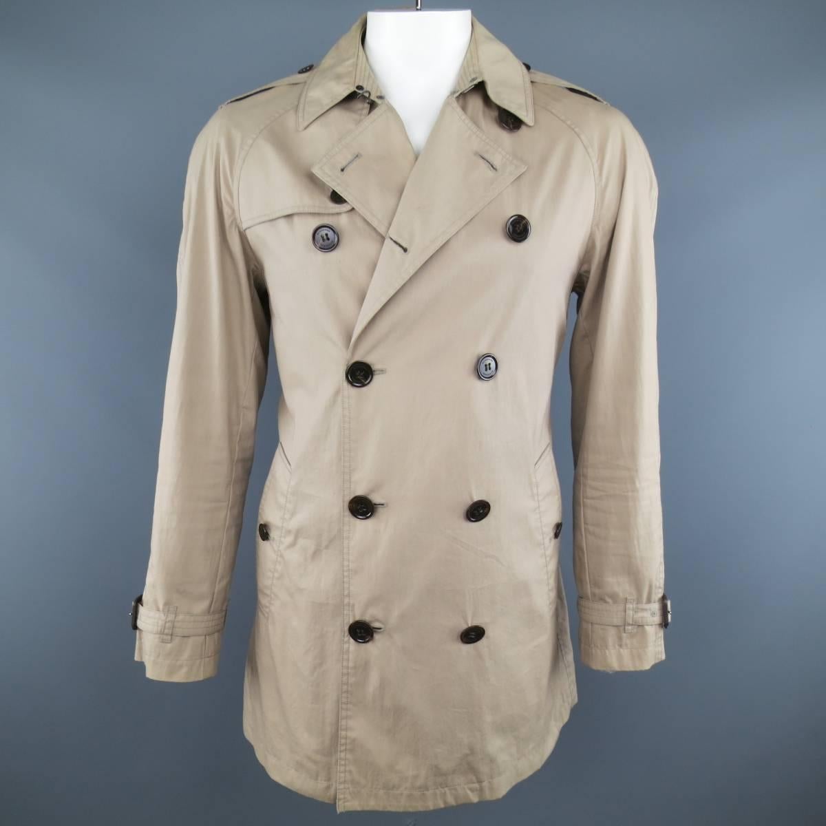 Classic BURBERRY BRIT trench coat comes in khaki cotton nylon blend canvas and features a pointed collar lapel, storm flap, double breasted button closure, belted waist, and raglan sleeves with epaulets. Wear throughout and discolorations shown in